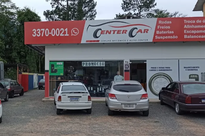 Fachada da Center Car em Corupá, com a placa vermelha, o telefone 3370-0021 e carros estacionados na frente